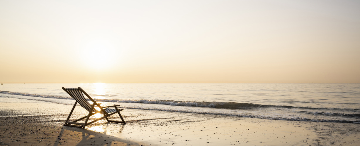 Empty folding chair on shore at beach against clear sky during sunset