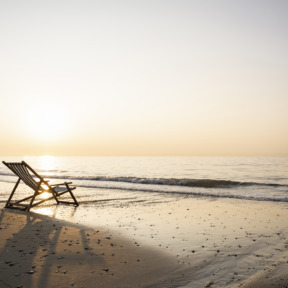 Empty folding chair on shore at beach against clear sky during sunset