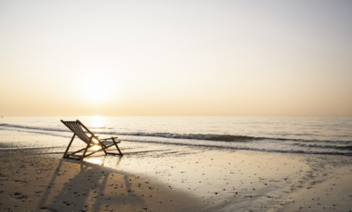 Empty folding chair on shore at beach against clear sky during sunset