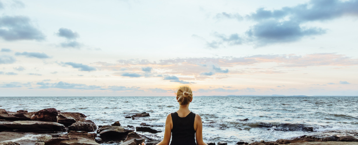 Young woman performs yoga moves on bluff above sea
