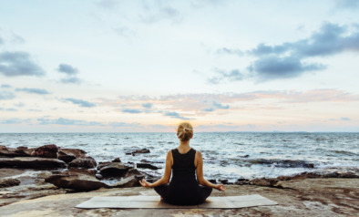 Young woman performs yoga moves on bluff above sea